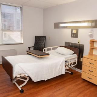 A clean and minimalist hospital room with a bed, chair, and dresser.