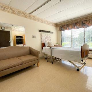 A cozy hospital patient room featuring a bed and a sofa, with large windows allowing natural light.