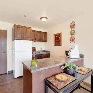A cozy apartment kitchen with wooden cabinets, a refrigerator, and a countertop with bar stools.