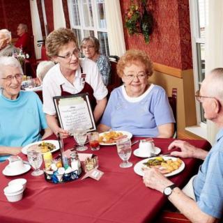A group of seniors enjoying a meal at a restaurant, served by a waitress.