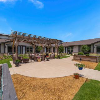 A well-maintained courtyard featuring a pergola with outdoor seating and landscaped gardens under a clear blue sky.