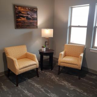 A cozy seating area featuring two yellow chairs, a side table with a lamp, and natural light coming through the windows.