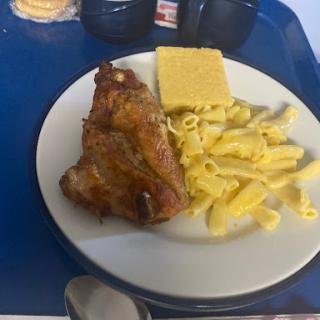 A hearty meal featuring roasted chicken, pasta, and cornbread served on a tray.