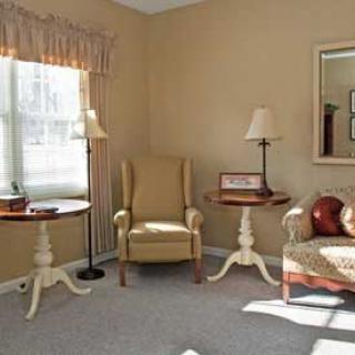 A cozy living room with armchairs and side tables, illuminated by natural light through a window.