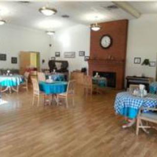 A spacious dining room with several tables and chairs, featuring a wooden floor and a fireplace with a clock above it.