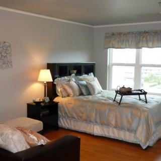 A cozy bedroom with a neatly made bed, bedside lamp, and a window letting in natural light.