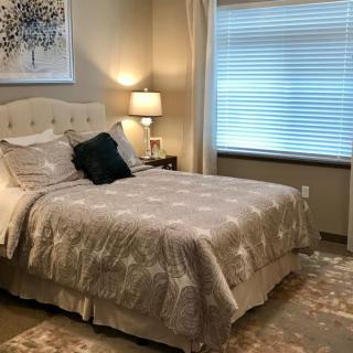 A cozy bedroom with a neatly made bed, a bedside lamp, and window blinds.