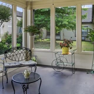 A cozy sunroom with wrought iron furniture and potted plants, bathed in natural light.