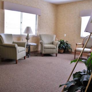 A cozy living room setting featuring two chairs, a lamp, and a window with sunlight filtering in.