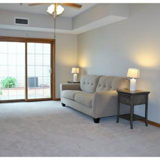 A cozy living room with a sofa and lamps, featuring neutral tones and a sliding glass door.