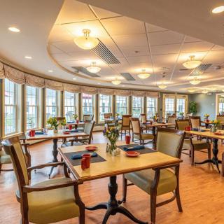 A well-lit dining room with neatly arranged tables and chairs, featuring large windows.