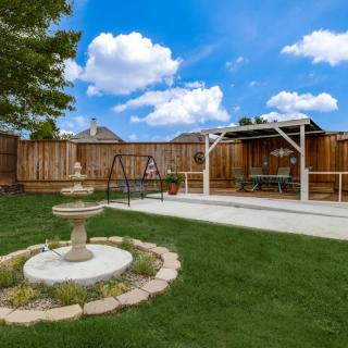 A serene backyard featuring a fountain, swing, and pergola on a sunny day.