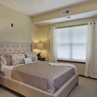 A cozy bedroom with a neatly made bed, lamp, and window with curtains.