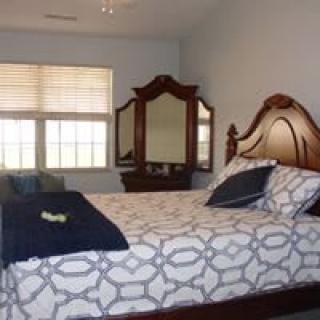 A cozy bedroom with a large bed, patterned bedding, and a wooden dresser with a mirror.