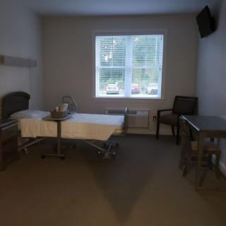 A simple hospital room with a bed, window, chair, and television.