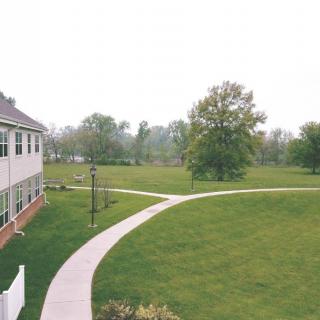 A scenic view of a building with a pathway curving through a grassy area surrounded by trees.