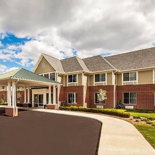 A modern two-story brick building with a covered entrance and landscaped surroundings under a cloudy sky.