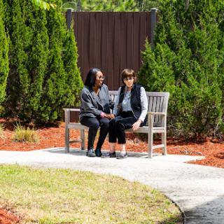 Two individuals engaged in a heartfelt conversation on a park bench surrounded by lush greenery.