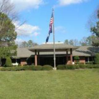 A building with flags in front, surrounded by a lawn and trees under a blue sky.