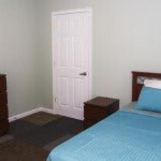 A minimalist bedroom with a neatly made bed, wooden furniture, and a closed door.