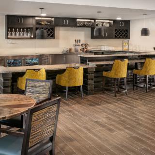 A modern bar with yellow chairs and a sleek counter, featuring wood flooring and a cozy atmosphere.