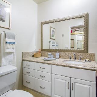 A bright and modern bathroom with white cabinets, a large mirror, and neatly arranged towels.