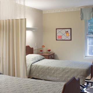 A hospital room with two beds and a privacy curtain, featuring a window and wall artwork.