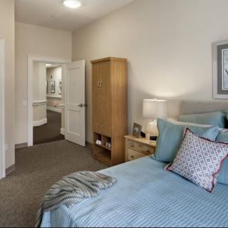 A cozy bedroom with a neatly made bed, a wooden wardrobe, and a bedside lamp.