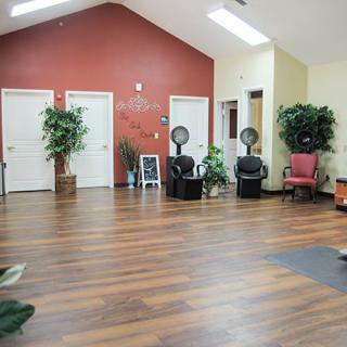 An empty salon interior with wooden flooring, styling chairs, and plants for decor.