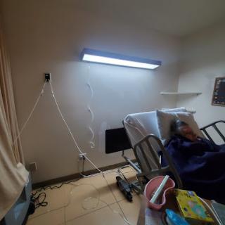 A hospital room with a patient resting in bed, equipped with medical supplies and overhead lighting.