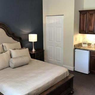 A cozy bedroom with a large bed, nightstand, and mini-fridge in the corner.