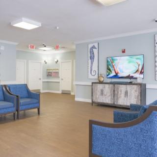 A modern waiting room with blue chairs and a television, featuring decorative wall art and wood flooring.