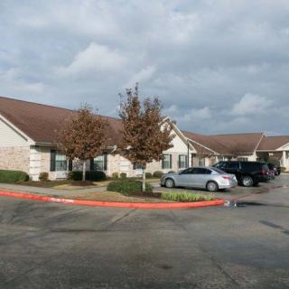 A suburban building with a parking lot and several cars parked under a cloudy sky.