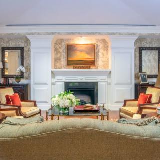 A cozy, traditionally styled living room featuring a central fireplace, elegant furniture, and tasteful artwork.