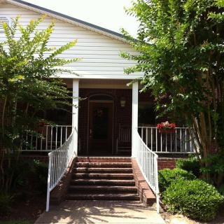 A welcoming house entrance with a brick staircase and porch, surrounded by greenery.