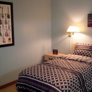 A cozy bedroom with patterned bedding, a wall-mounted lamp, and guitar-themed artwork.