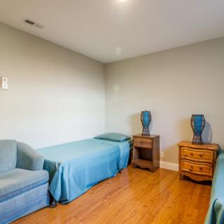 A minimalist bedroom featuring two twin beds with blue covers, a wooden floor, and decorative vases on bedside tables.
