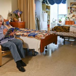 An elderly person is sitting in a cozy nursing home room, reading a book.