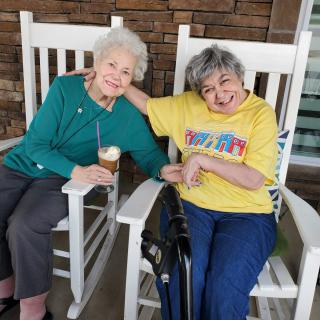 Two elderly women smiling and sitting in rocking chairs, enjoying each other's company.