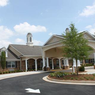 A well-maintained building with a circular driveway and landscaped gardens under a blue sky.