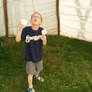 A young boy joyfully enjoying ice cream inside a tent.