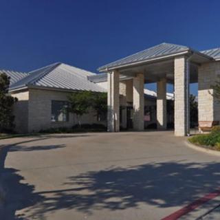 A large building with a prominent entrance and a driveway under a clear blue sky.
