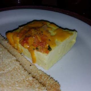 A delicious egg casserole topped with cheese, served with a slice of toast.
