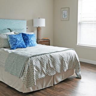 A cozy bedroom with a neatly made bed featuring blue pillows and a bedside table with a lamp.
