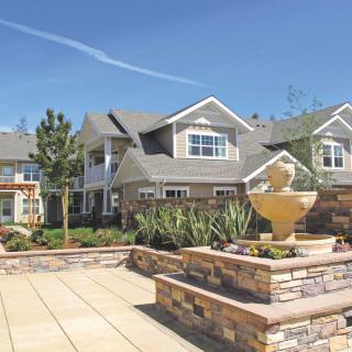 A beautiful house with a stone fountain and landscaped surroundings on a sunny day.