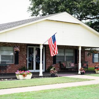 A charming home displaying an American flag, surrounded by a well-maintained front yard and colorful flower pots.