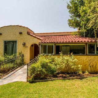 A charming single-story house with a tiled roof, surrounded by lush greenery and a well-maintained garden.