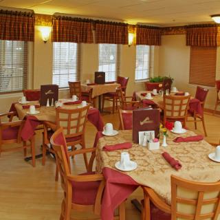 A cozy dining room with well-arranged tables and chairs, featuring elegant table settings and warm lighting.
