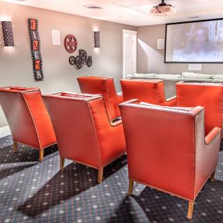A cozy home theater room with red chairs facing a large screen, complete with projector and stylish decor.