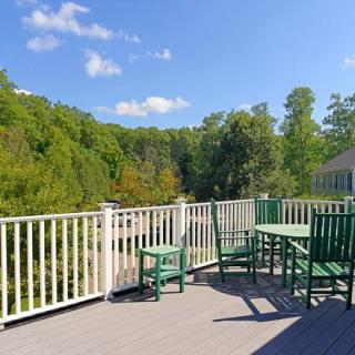 A sunny outdoor deck with green furniture overlooking a lush, tree-filled landscape.